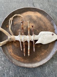 Metallnaeltest ja puidust meisterdatud kalakujuline ripats, mis asetseb roostekarva taldrikul